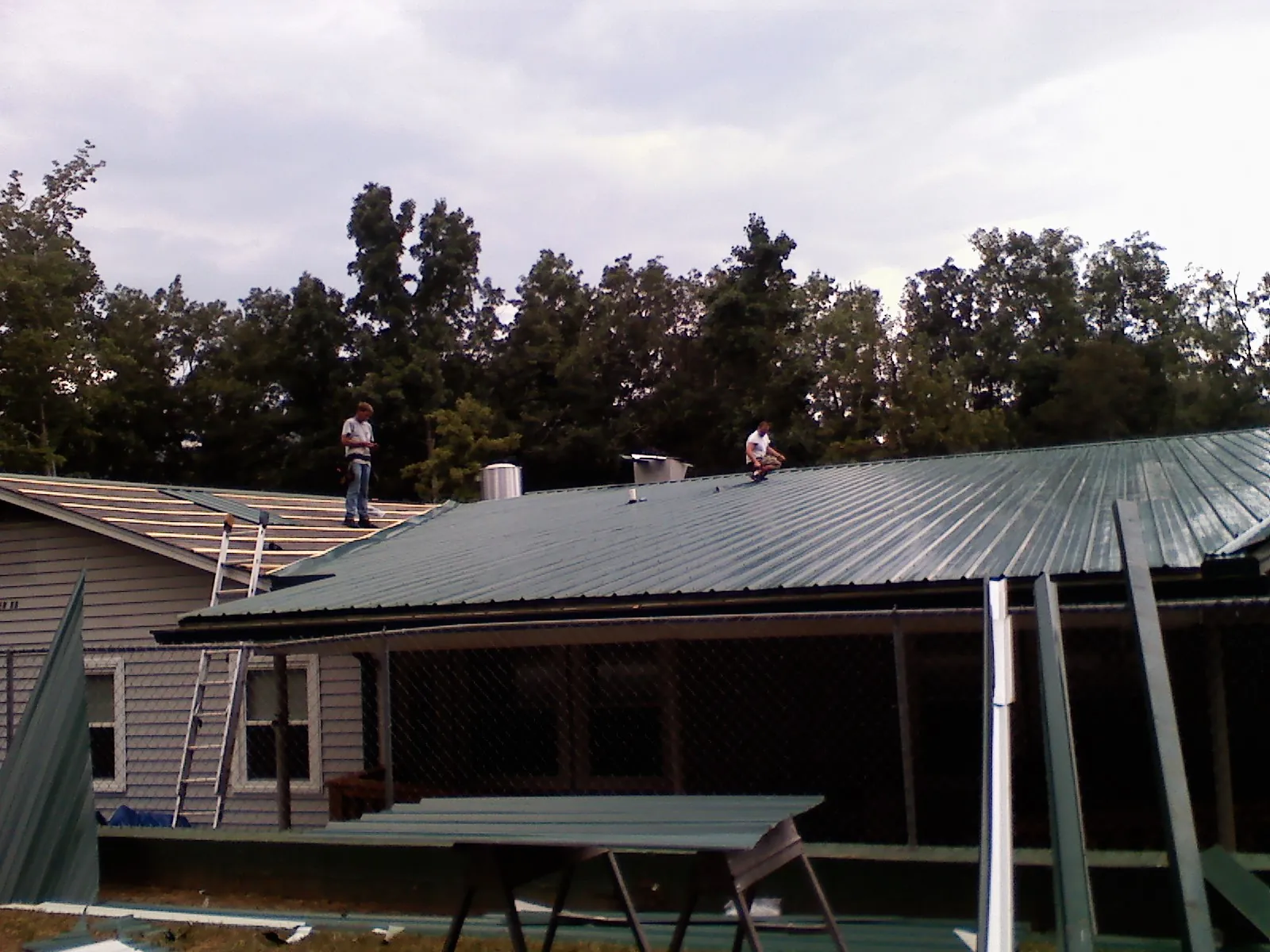 Two roofers installing green metal panels above a covered porch in Smyrna