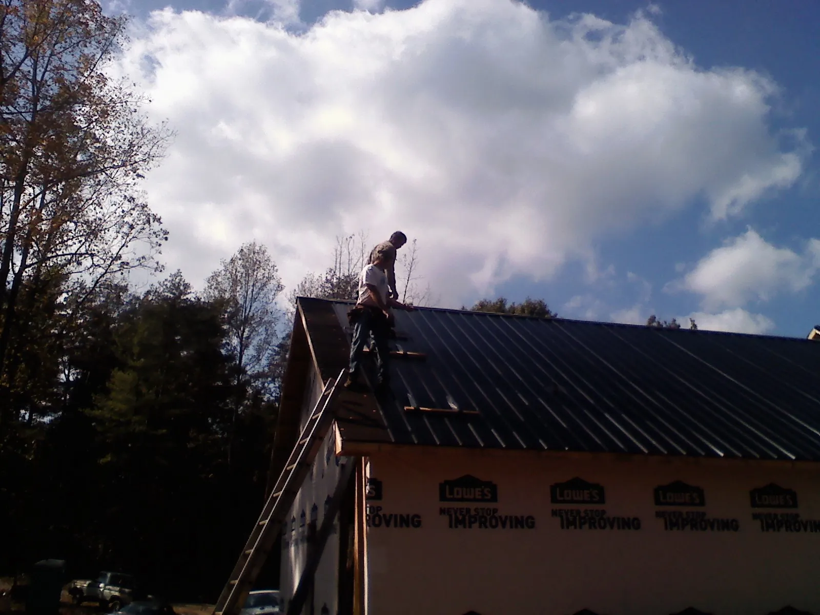 Roofer fastening dark metal panels high against a cloudy sky, from a Roof Inspection job in Smyrna